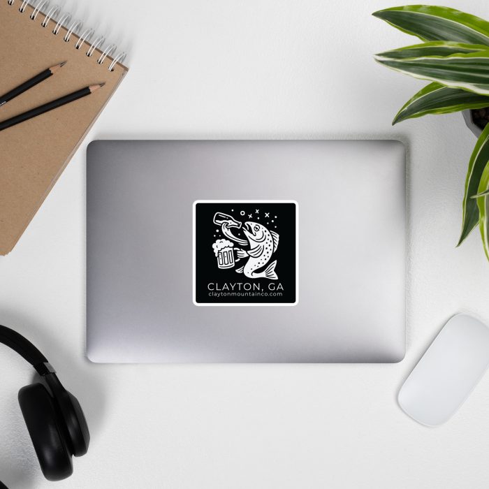 die-cut-stickers-satin-4x4-front-6a2e9f7335c17jpg - Clayton Mountain Co. Top-down desk scene with a closed laptop in center, a spiral notebook and two pencils on the left, headphones bottom-left, a white mouse bottom-right, and a green plant on the right; sticker on laptop reads 'Clayton, GA' with a graphic.