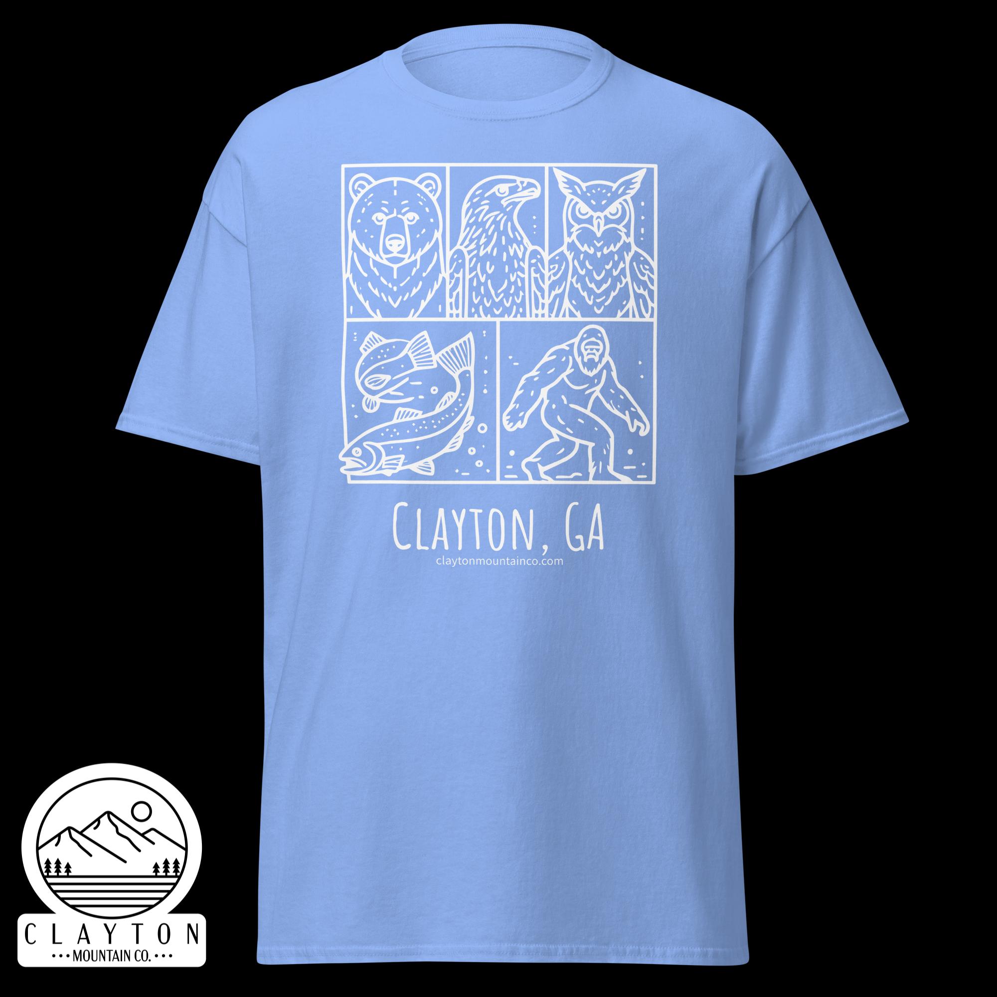 unisex-classic-tee-carolina-blue-front-6a2e6635a5debjpg - Clayton Mountain Co. Light-blue T-shirt with a white comic-style panel showing a bear, an eagle, and an owl; below is ‘Clayton, GA’ with a mountain logo.