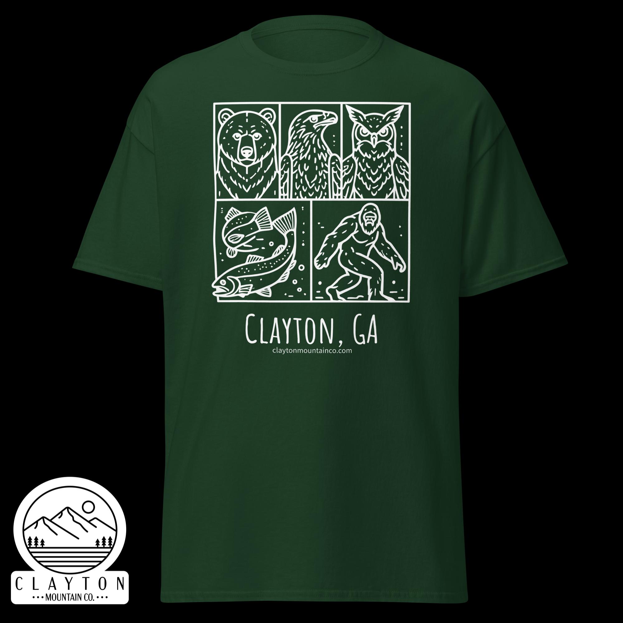 unisex-classic-tee-forest-green-front-6a2e6635b388cjpg - Clayton Mountain Co. Green t-shirt featuring a white comic-style panel design with a bear, eagle, fish, and hiker, plus ‘Clayton, GA’ branding and mountain sticker.