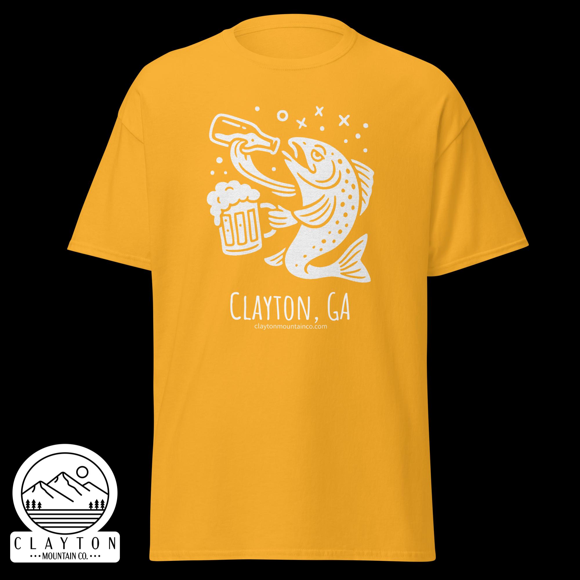 unisex-classic-tee-gold-front-6a2e5d89a100fjpg - Clayton Mountain Co. Yellow T-shirt with a white graphic of a fish holding a beer mug and splash marks; round sticker with a mountain scene and text 'Clayton Mountain Co.' beside the shirt.